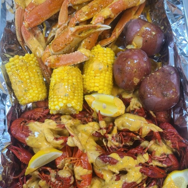 A seafood boil with crab legs, crawfish, corn on the cob, and red potatoes in a foil pan.