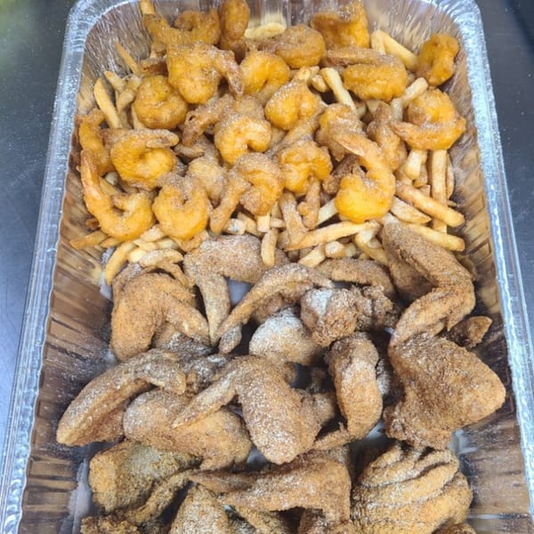 A catering tray filled with golden-brown fried shrimp, french fries, and seasoned chicken wings.